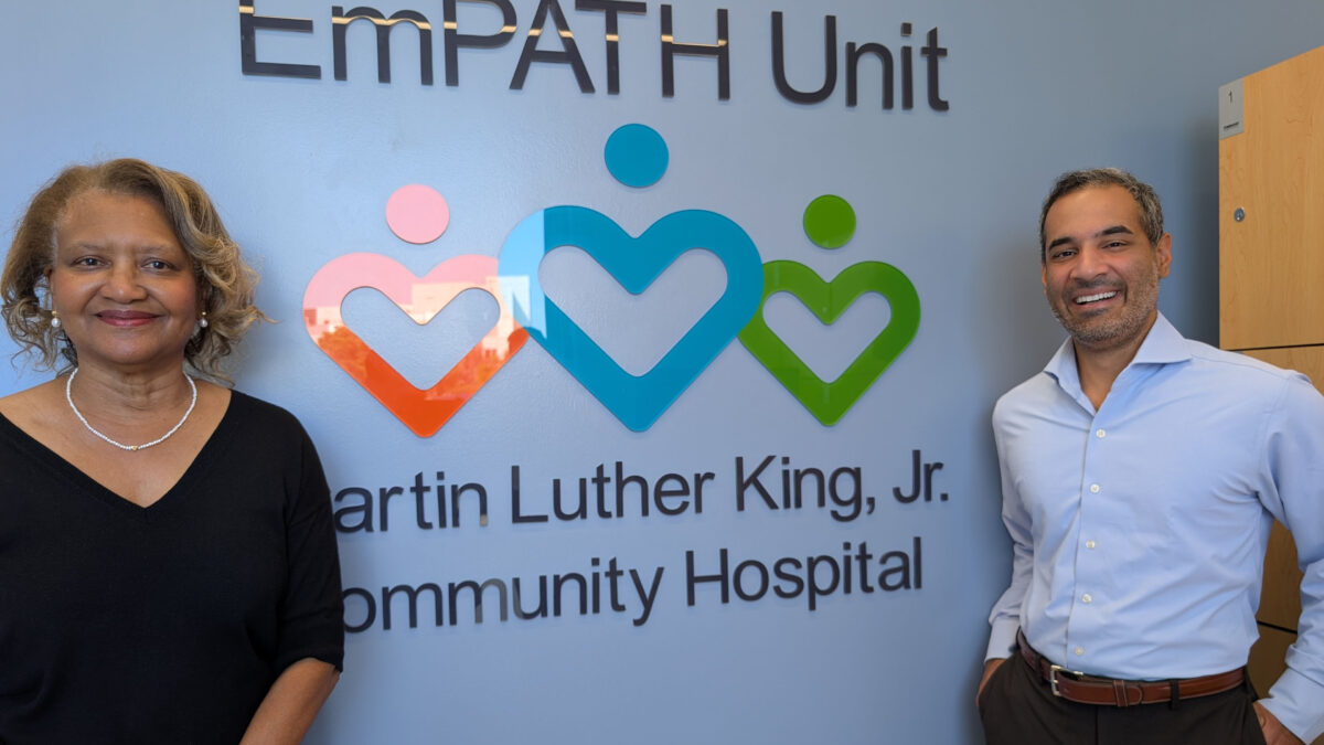 A woman and a man in business formal attired stand on either side of a sign that says, "EmPATH Unit / Martin Luther King Jr. Community Hospital."