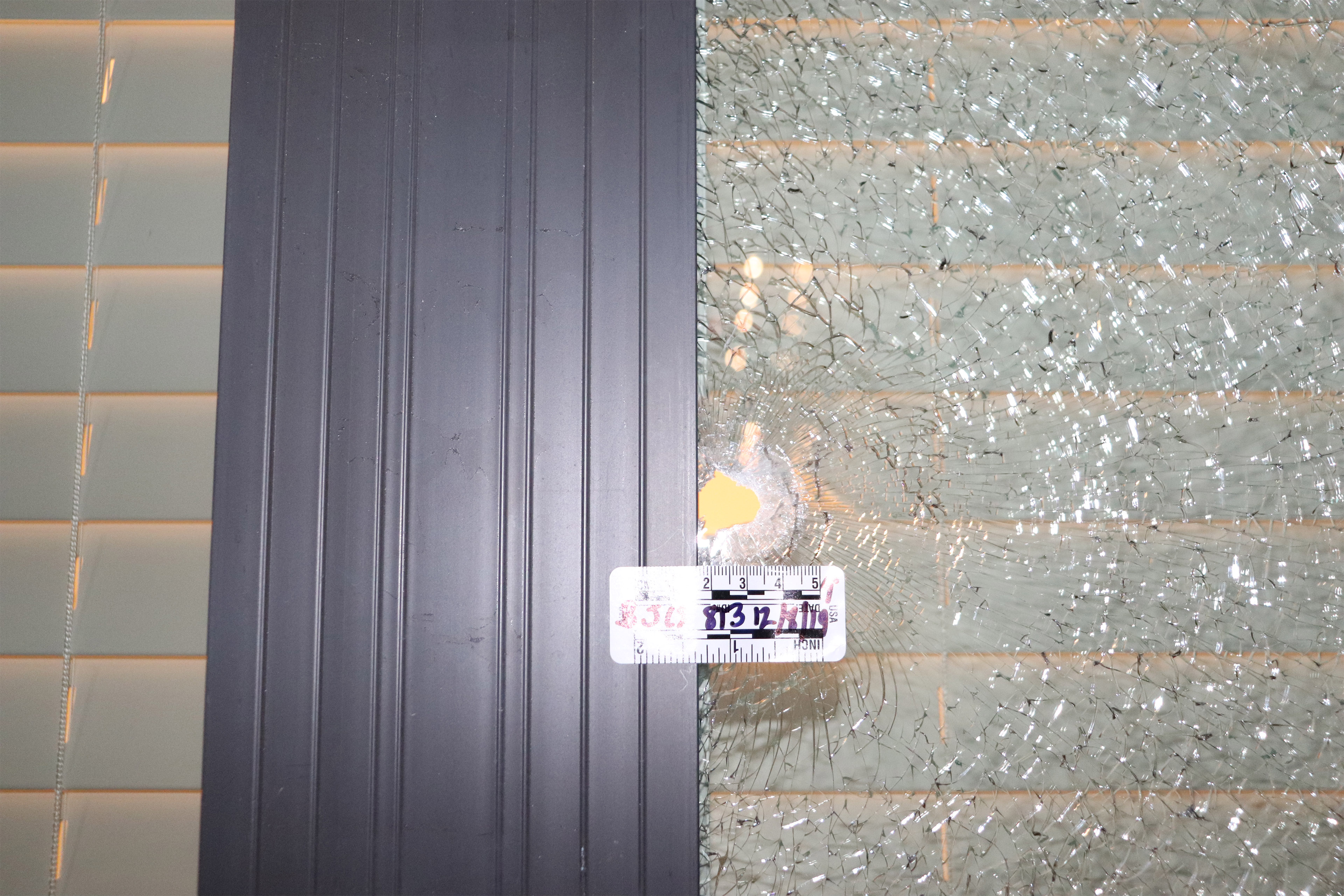 A close-up photo of a window with a bullet hole and fractured glass.