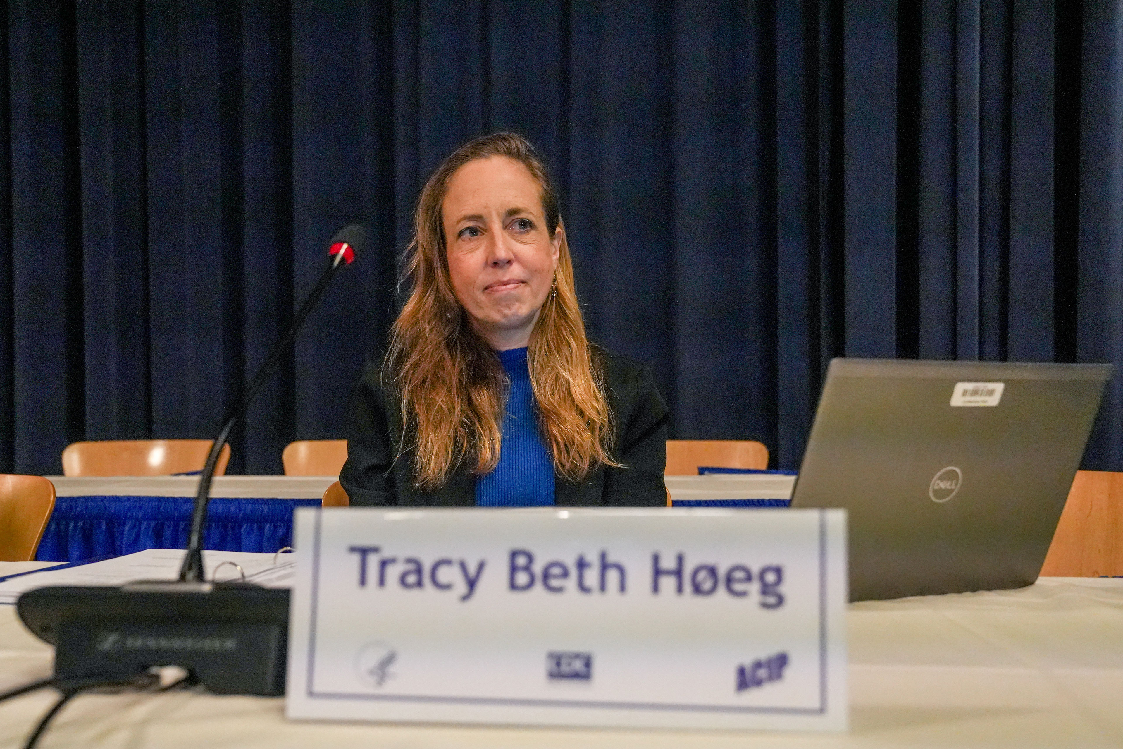 Tracy Beth Høeg sits at a table, a microphone and nameplate in front of her. A laptop is on the table to her left.