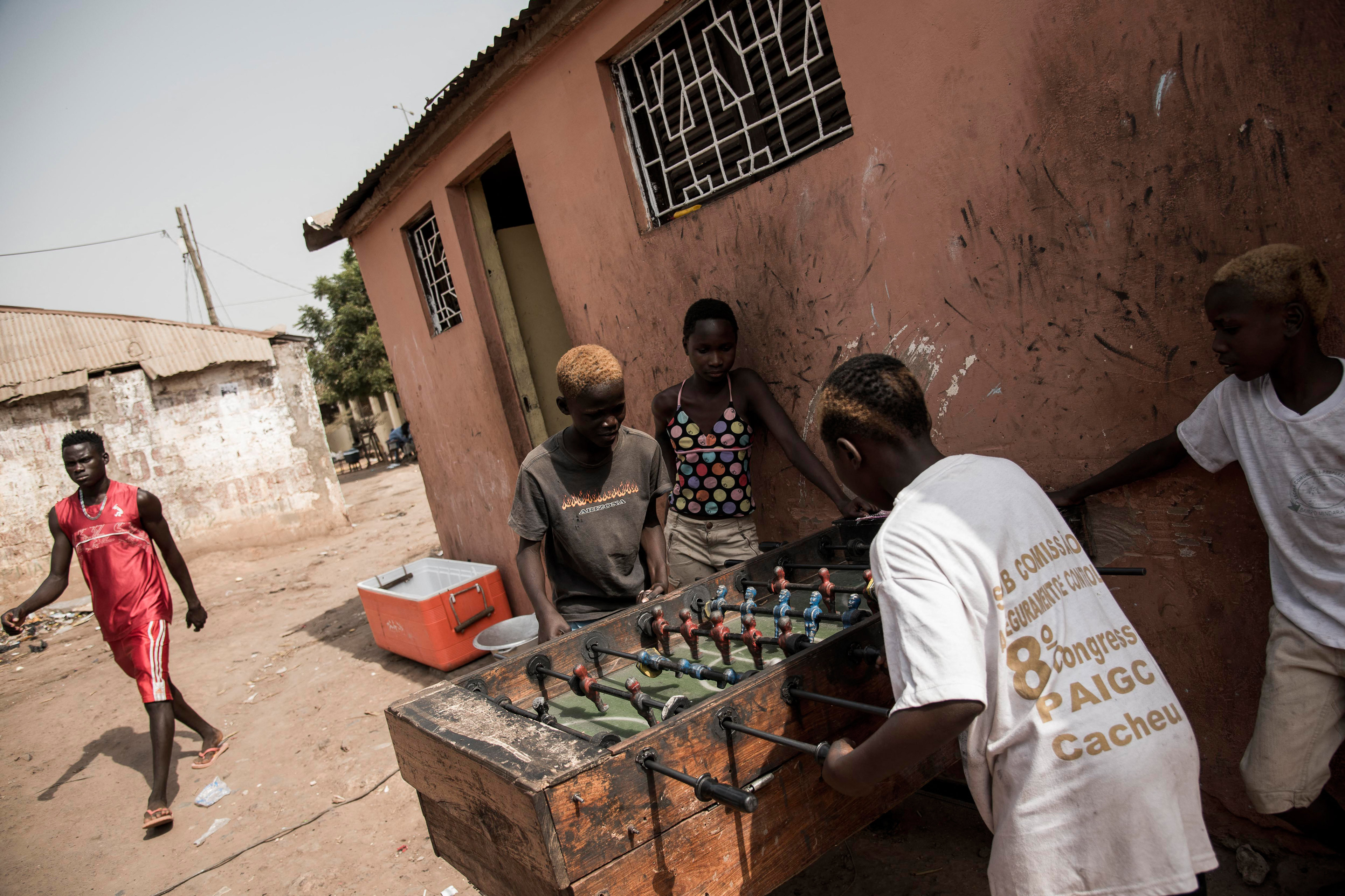 A photo of two kids playing foosball as two others watch. A fifth walks by on the left.