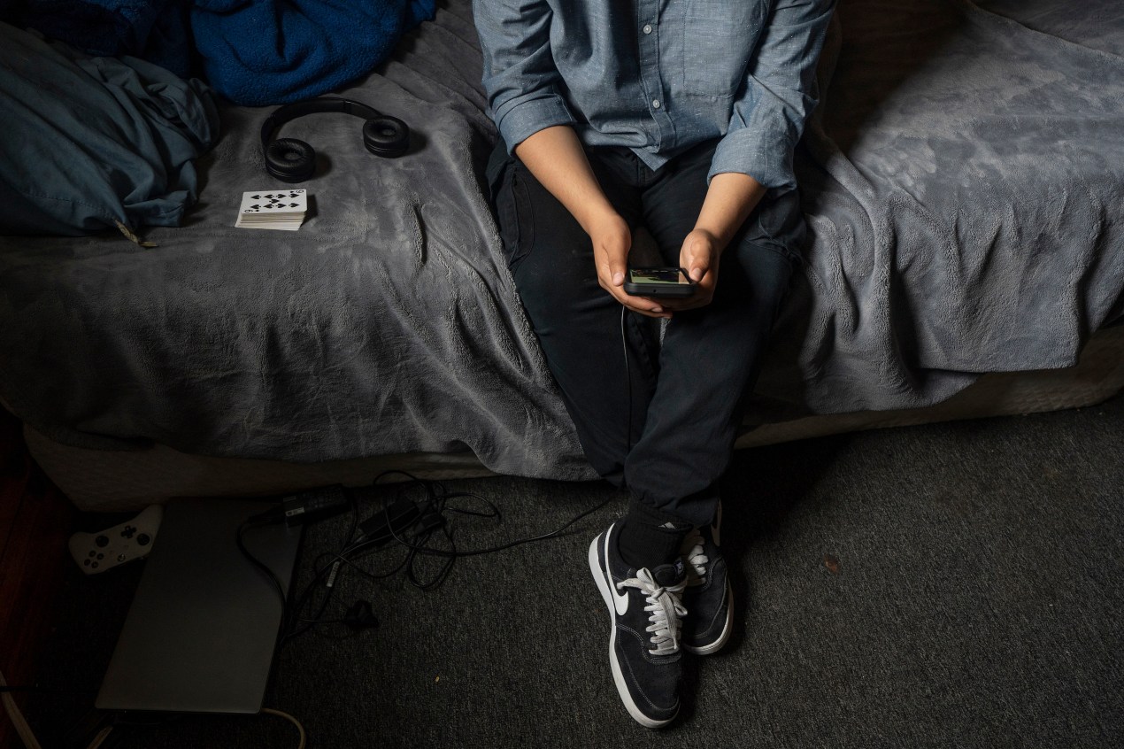 growing-up-scared-mental-health-03-web A person holds a smartphone as they sit on a bed
