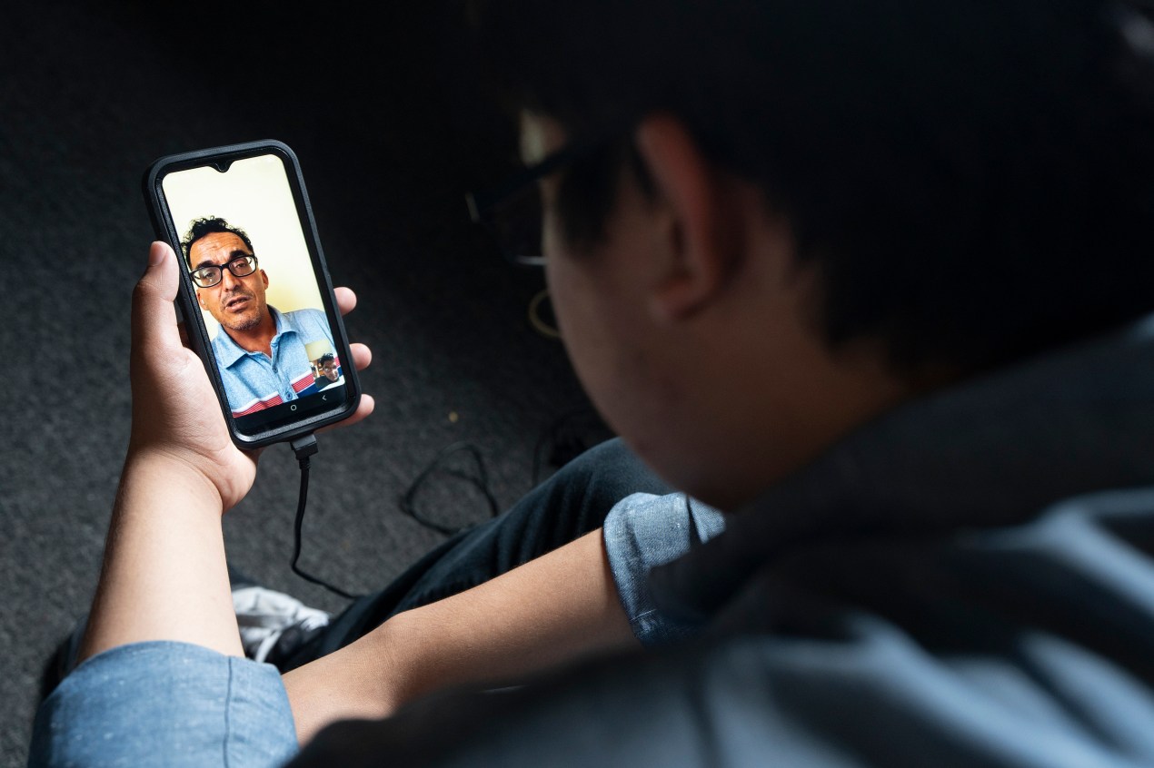 growing-up-scared-mental-health-06-web A man holds a smartphone with an image of a video chat with another man