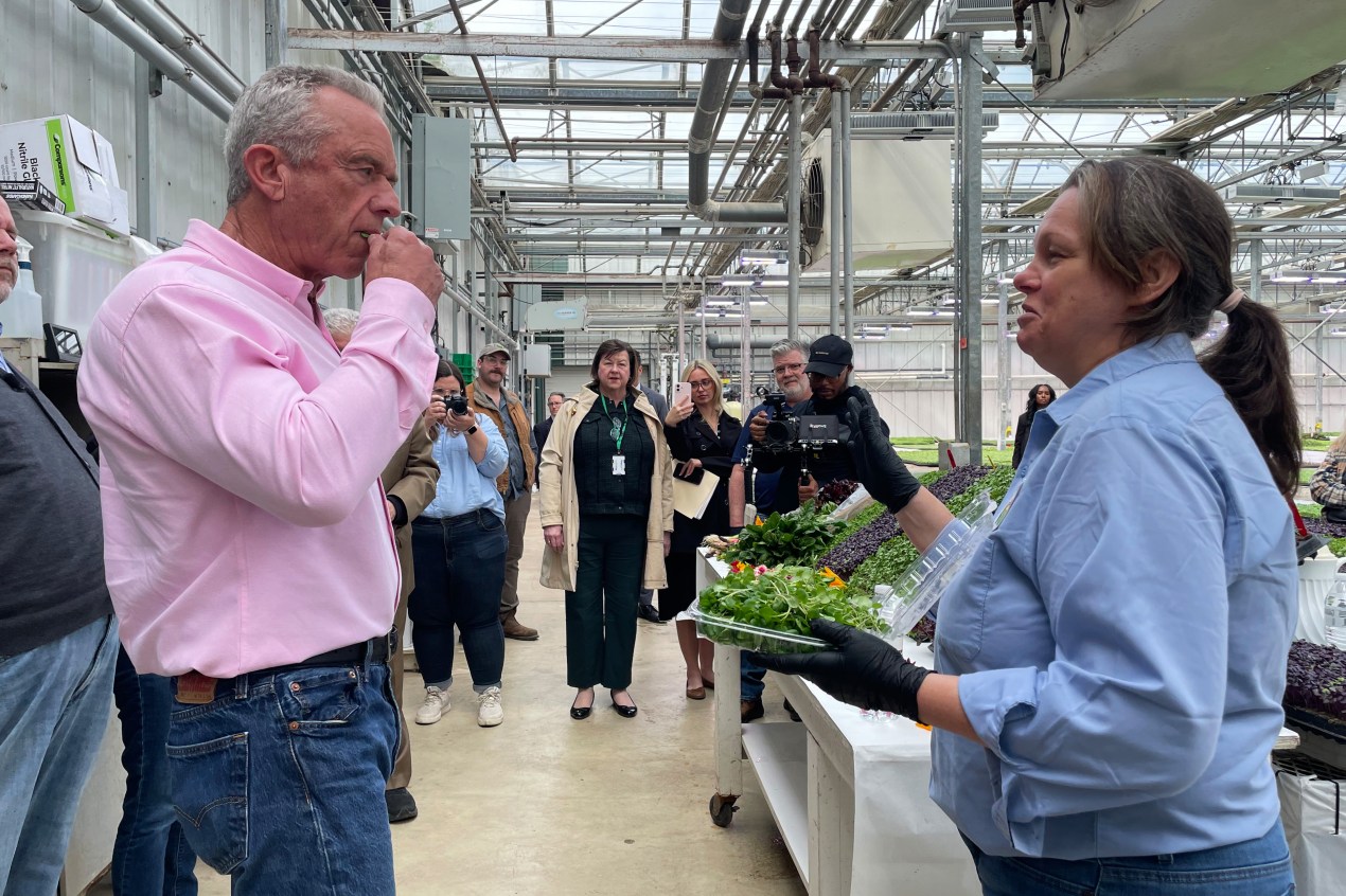 Robert F. Kennedy Jr. takes a bite of microgreens at a facility indoors.