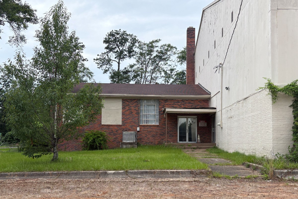 An exterior photo of a brick building attached to a larger white building.