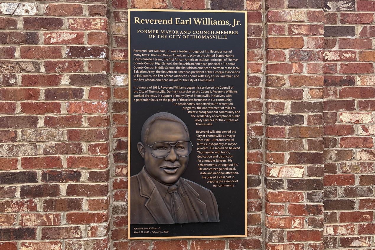 A plaque on a brick wall with the name and biography of Rev. Earl Williams Jr. The plaque also has a bas-relief sculpture of Williams.