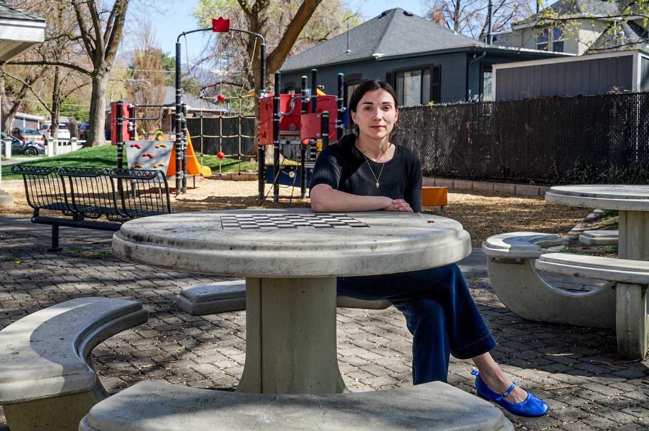 utahmeasles_01 A woman sits at a table in front of a children's playground.