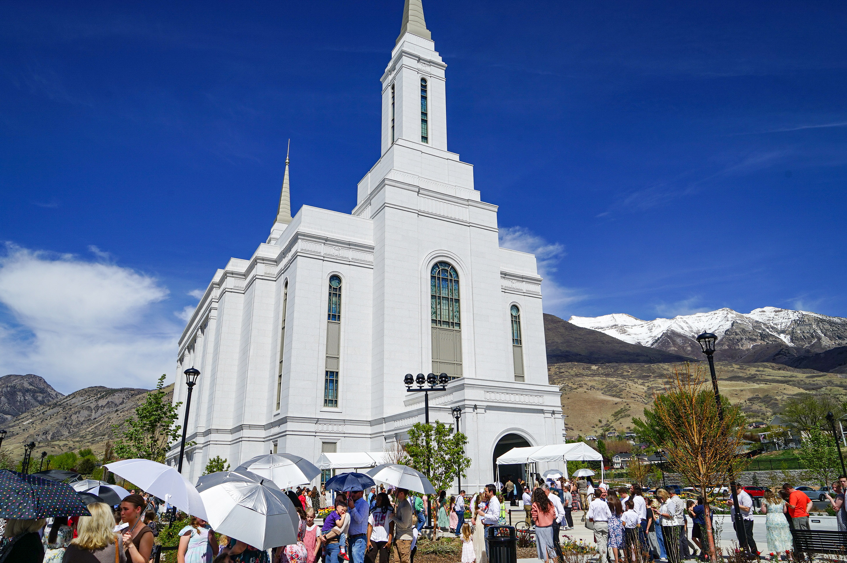 utahmeasles_10 A photo of an LDS temple: a large white church. People are gathered in front of it, some of them holding umbrellas to protect from the sun.
