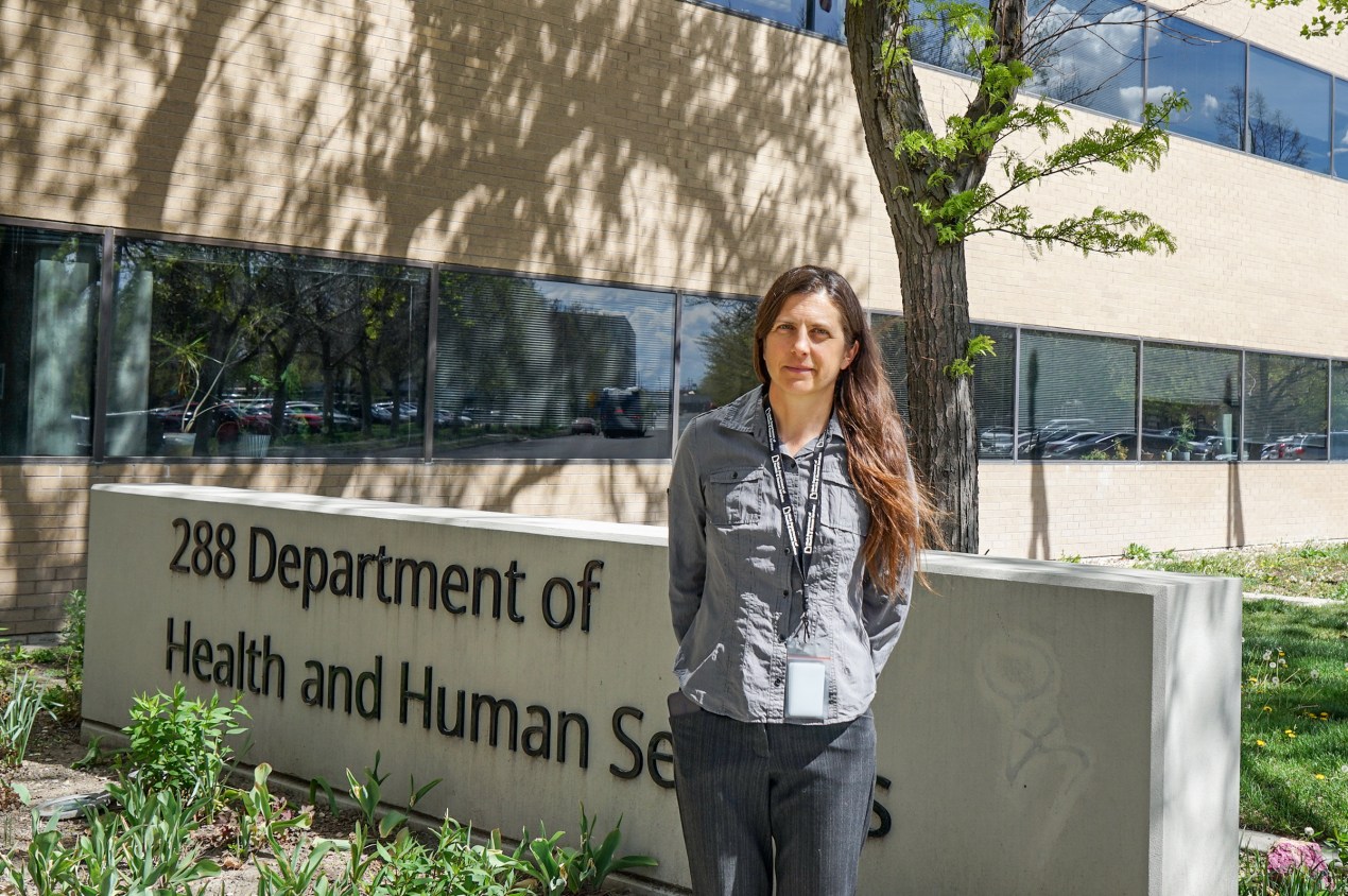 utahmeasles_11 A woman stands outside a building. A sign next to her reads, "288 Department of Health and Human Services."