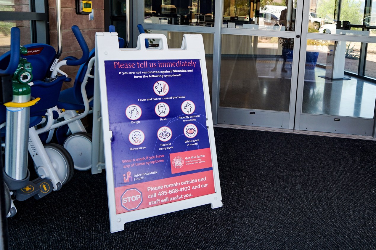 utahmeasles_12 A sign in front of a hospital reads, "Please tell us immediately if you are not vaccinated against Measles and have the following symptoms: fever and two or more of the below — cough, rash, recently exposed to measles, runny nose, red and runny eyes, white spots in mouth."