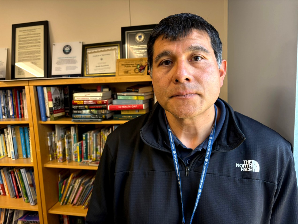 A portrait of a man wearing a black shirt standing in front of a bookcase