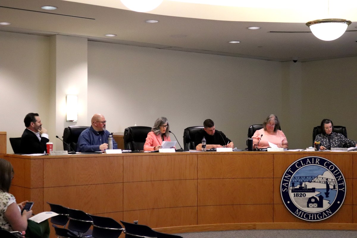Six members of a board sit at a desk with signage that says "Saint Clair County, Michigan"